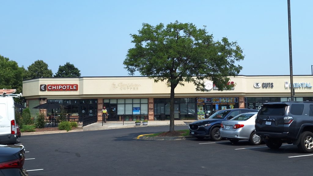 A strip mall with a noticeable gap between a Chipotle and the business next to it. Remains of a faded Caribou Coffee logo are visible between the stores.