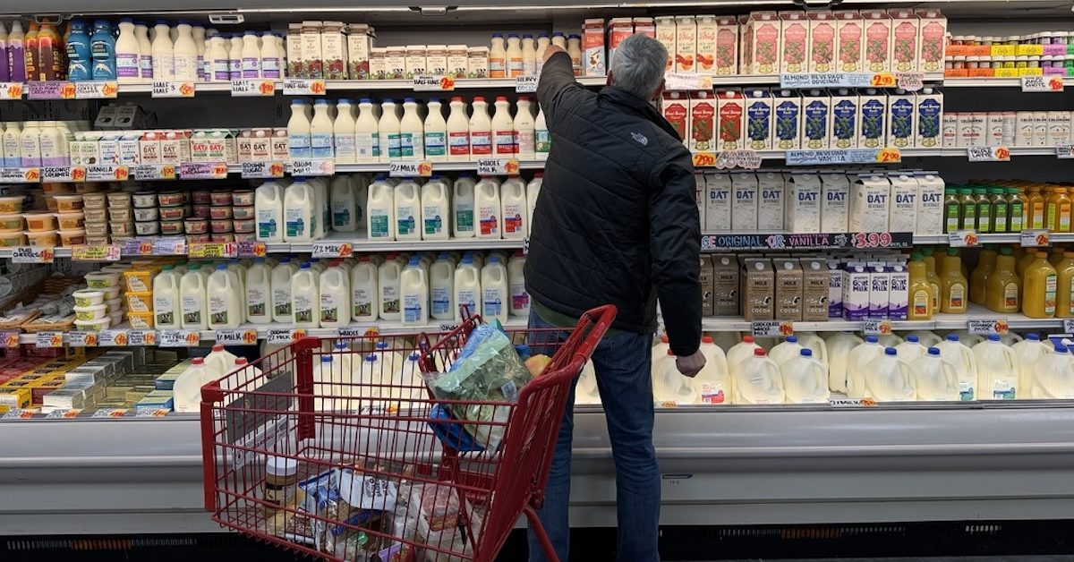A person reaches for a container of milk in the dairy section of a grocery store.