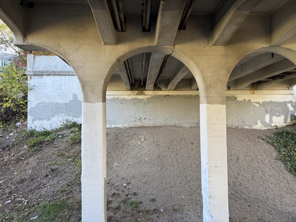 Two concrete piers are visible, and are equally shaped in width and depth. They form a comparatively smaller arch above into the bridge.