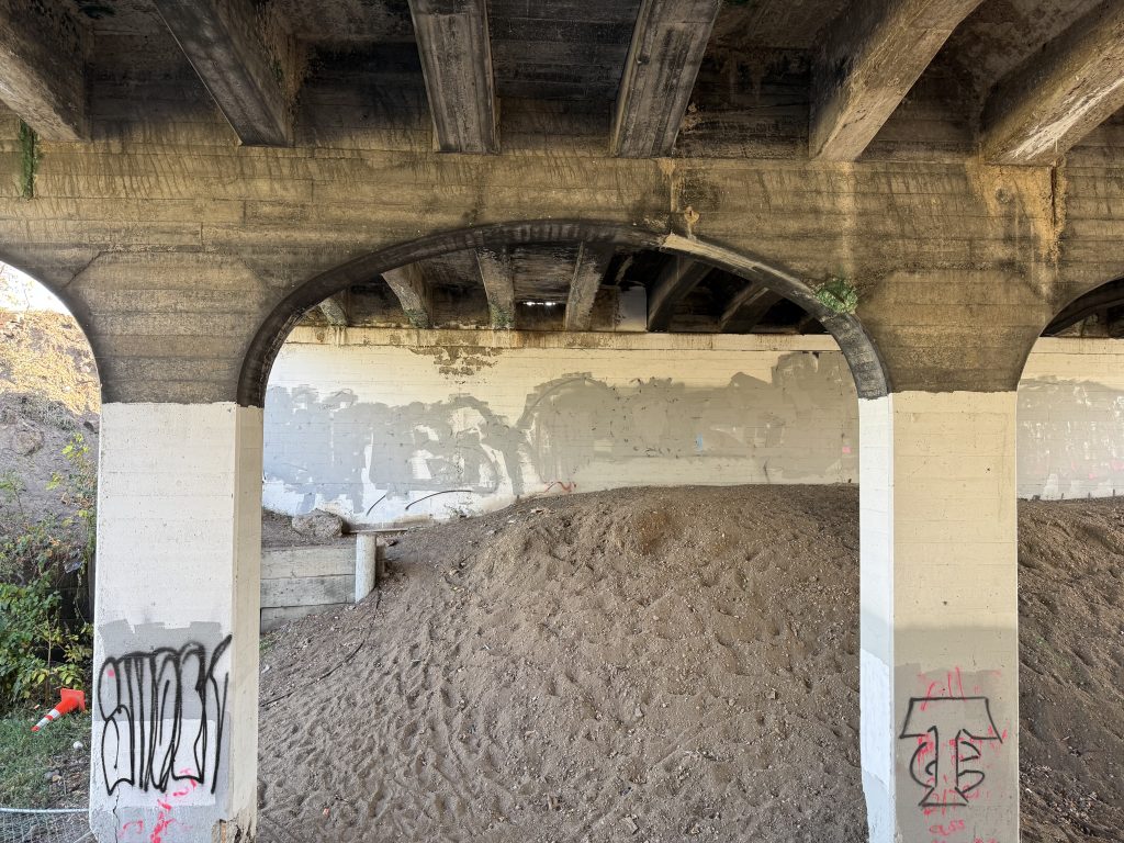 Two concrete piers are visible, and are wider than they are deep. A wide arch joins the two piers. Imprints of the wood forms used for the concrete are visible on the underside of the bridge.