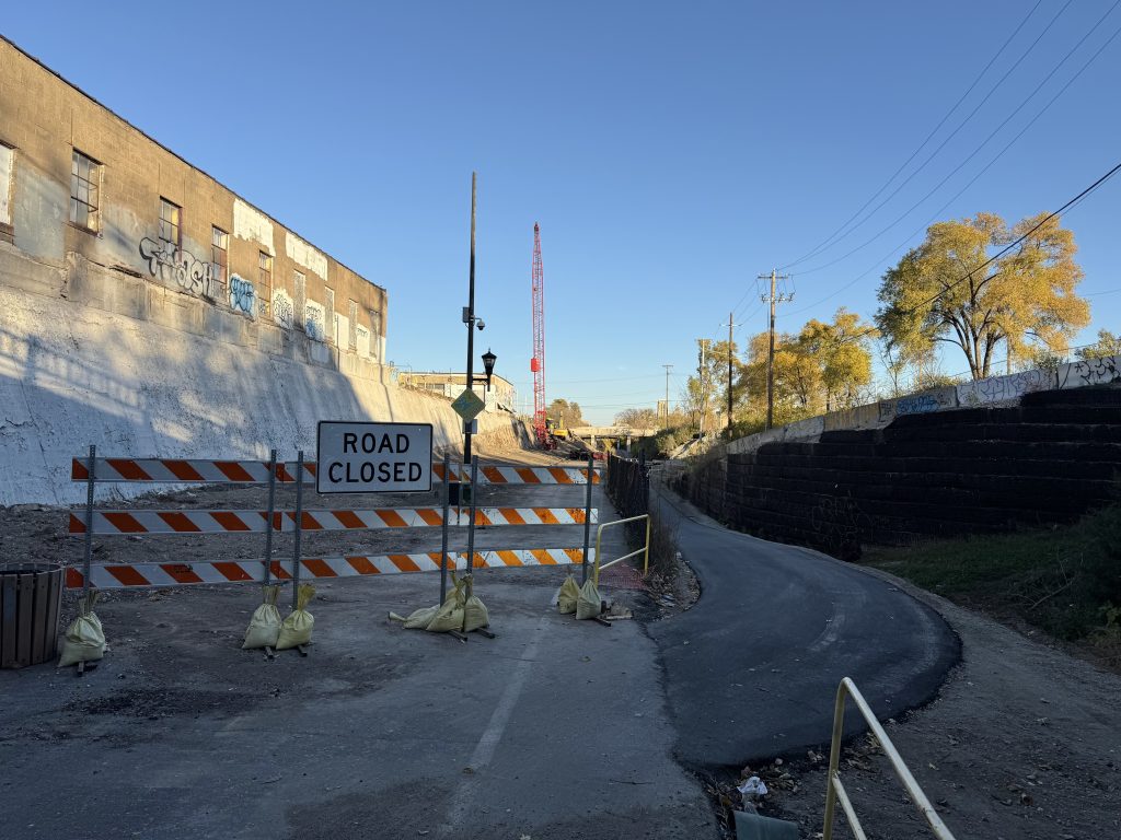 A road closed sign blocks the trail on the Midtown Greenway. A more narrow fresh asphalt path veers off of the trail into the lower utility path of the corridor.