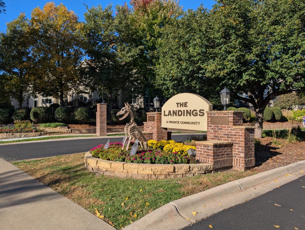 suburban style entry and exit roads with signage and planting in between supplemented by a decorative skeleton of a dog
