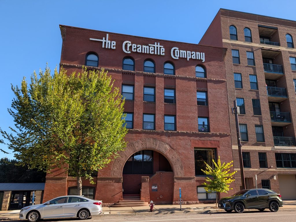 building in red brick and rusticated stone with roman entry arch, arched windows on top floor, and signage for the Creamette Company