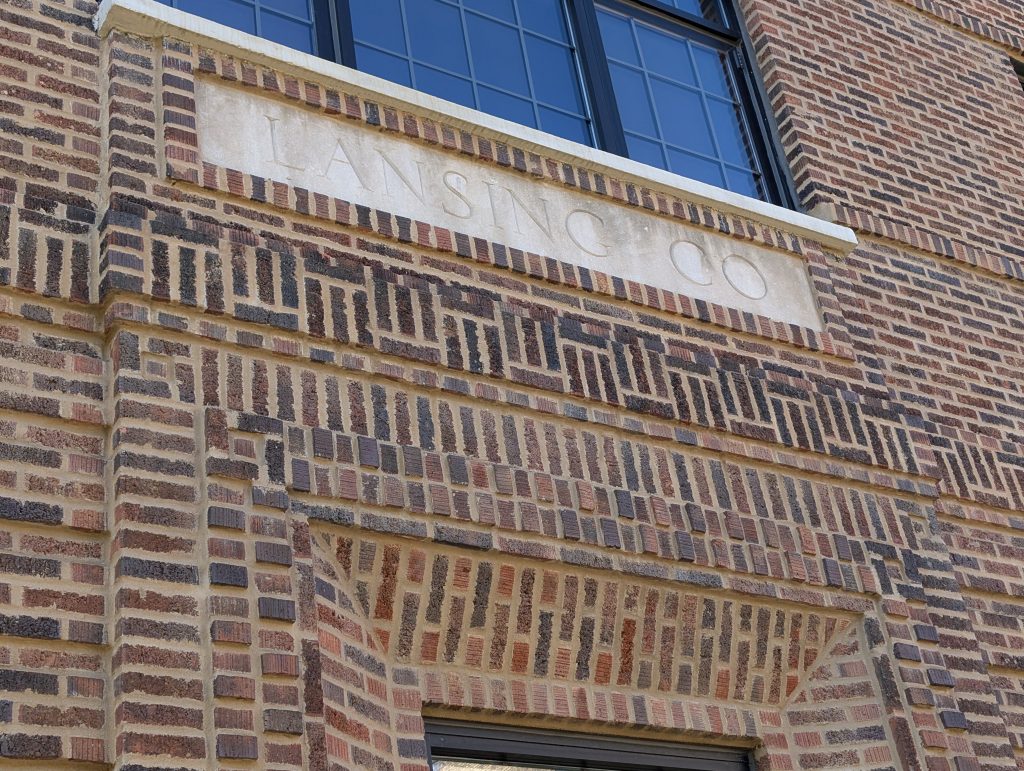 detail of red/brown brick building showing fancy brickwork including surrounding door and "LANSING CO" nameplate