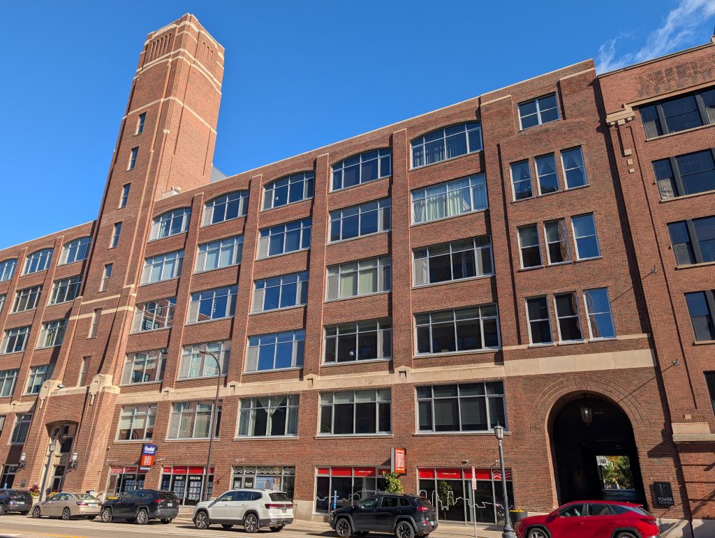 red brick building with contrasting string course above second floor, central tower, and arched passageway with lantern