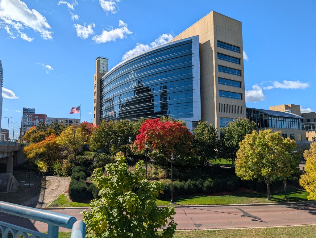 building featuring curved glass wall with autumnal tree-lined parkway in foreground