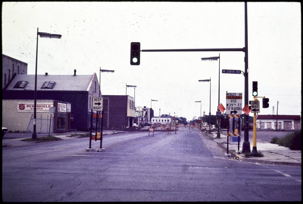 Looking south along Nicollet Ave with road closure and detour signs posted. The slight curve of the Nicollet Ave bridge is visible in the distance, and past it, the street lights are still up in the location where the Kmart will be built.
