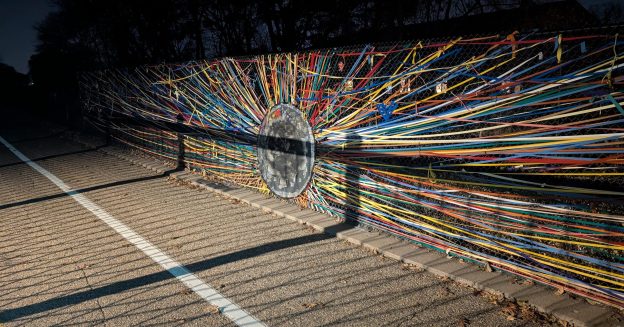 A colorful piece of ribbon art on a chain link fence.