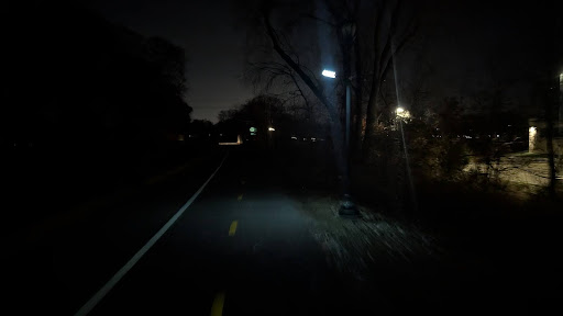 A similar view of the Midtown Greenway as the previous photo, now very dark, with the solar lamp shedding a small pool of light.