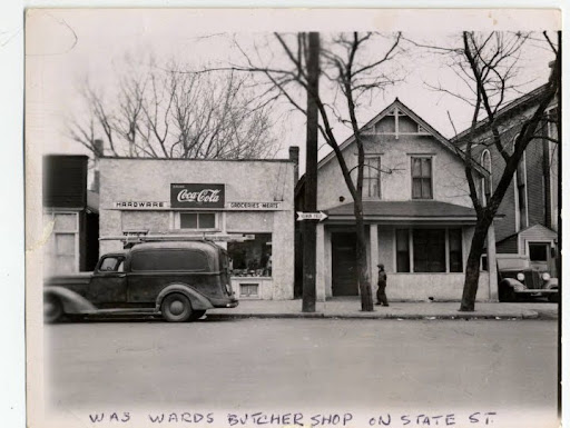 A hardware and grocery store next to residential house, with a car out front. 