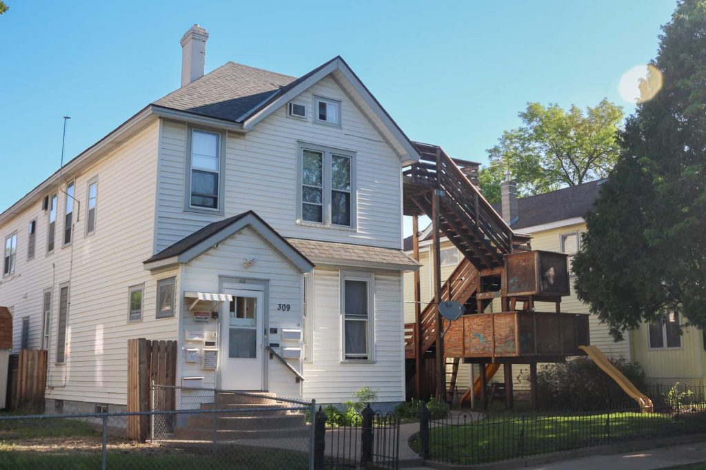 A multilevel home with white siding and seven mailboxes on the front of the house and a set of wooden steps combined with a children's play area on the side.