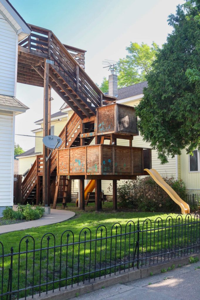 A series of wooden steps that lead up to the second level of the home, with two slides and a small play area including two slides built in on the lower level and a deck on the second level.