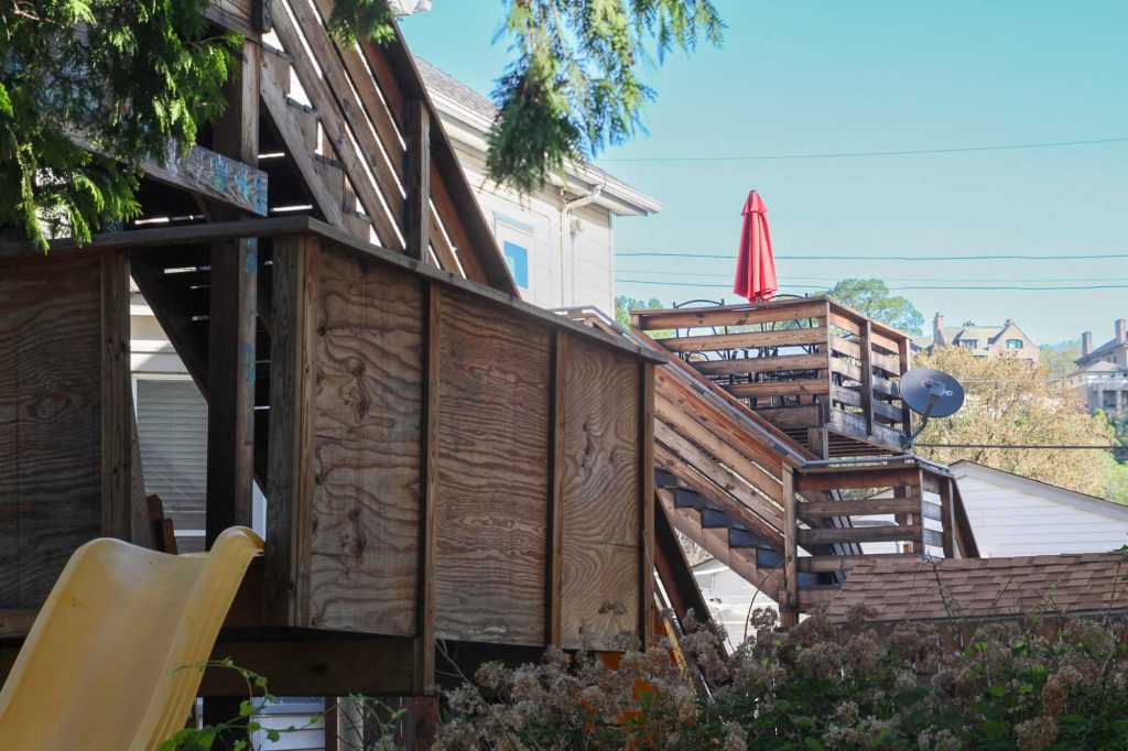 A deck with chairs, a table and umbrella behind the children's play area including a yellow slide and another wooden platform.