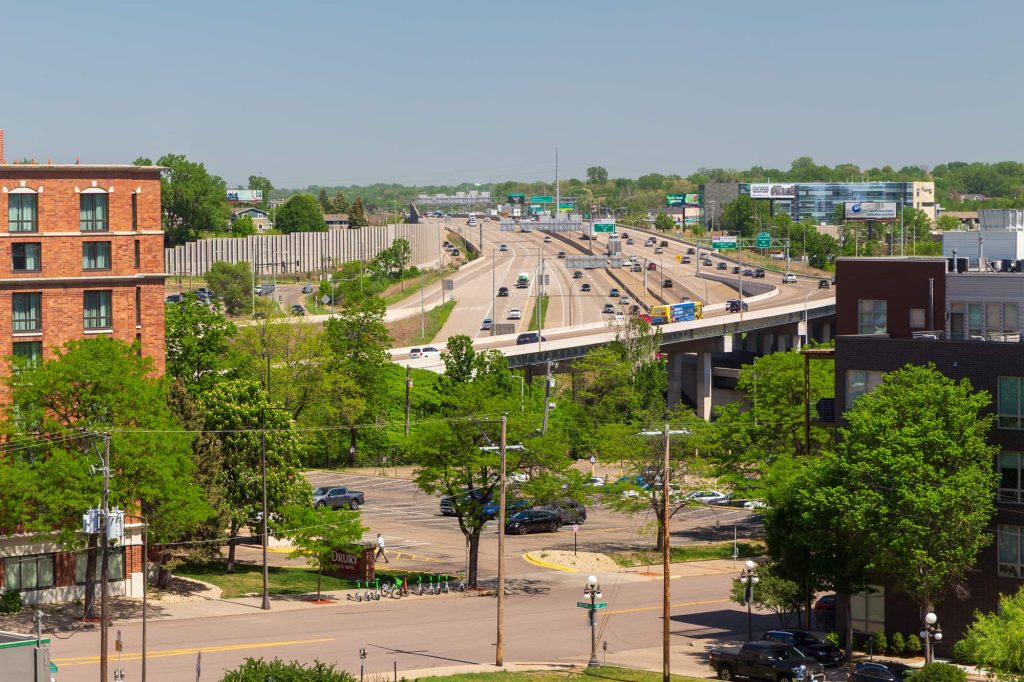 Street, parking lot and trees in front of the Interstate 94-35E junction.
