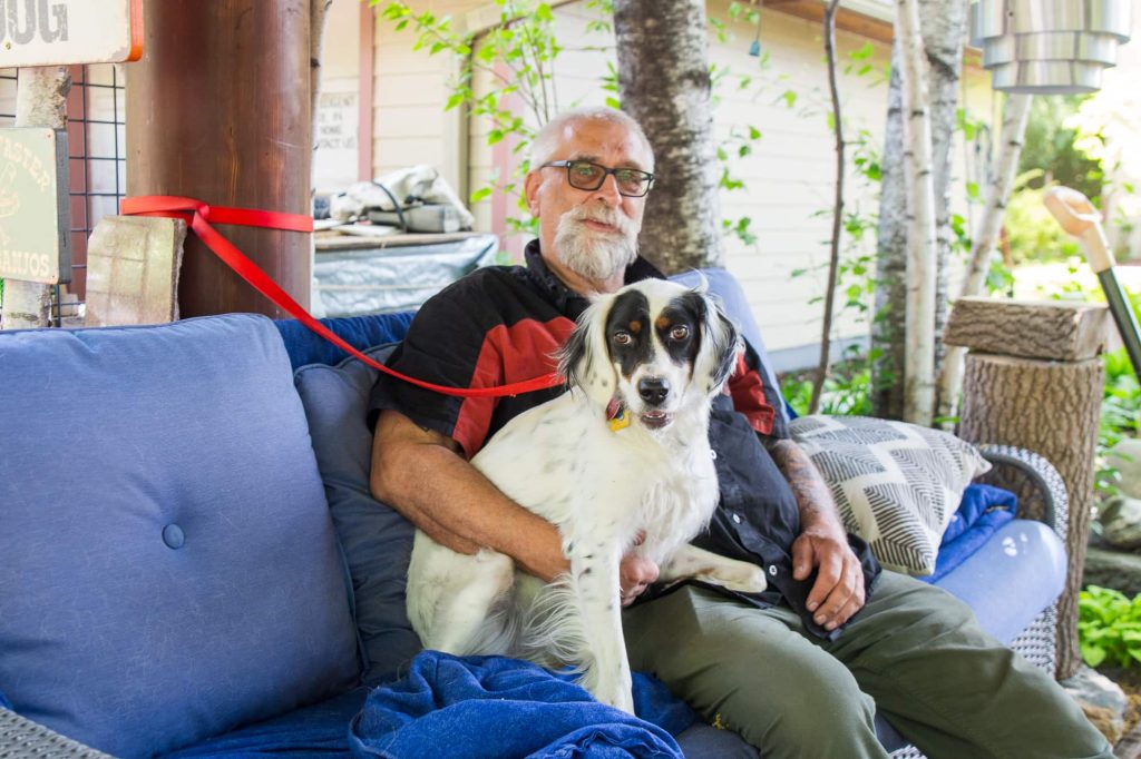 Doug and his dog, Nova, sit on a couch outside.