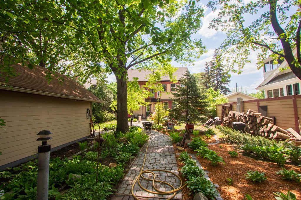 A cobblestone path with landscaped plants on either side and a garden hose on the walk.