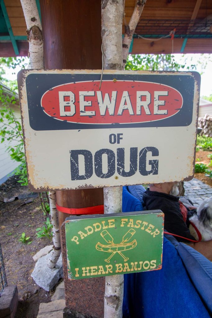 Two signs which read "Beware of Doug" and "Paddle Faster I Hear Banjos."