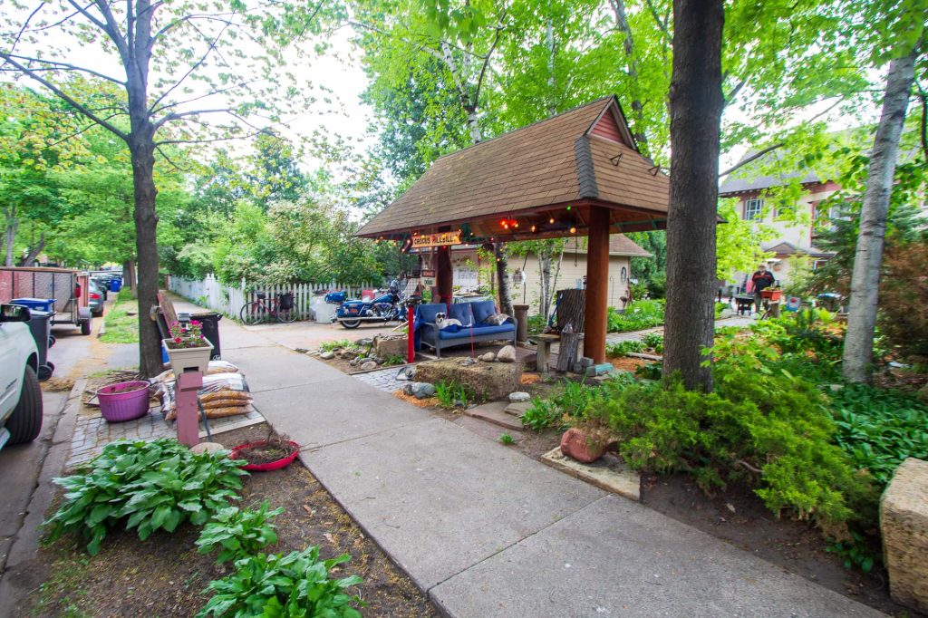 A pagoda with string lights and a blue couch in the backyard near the sidewalk.