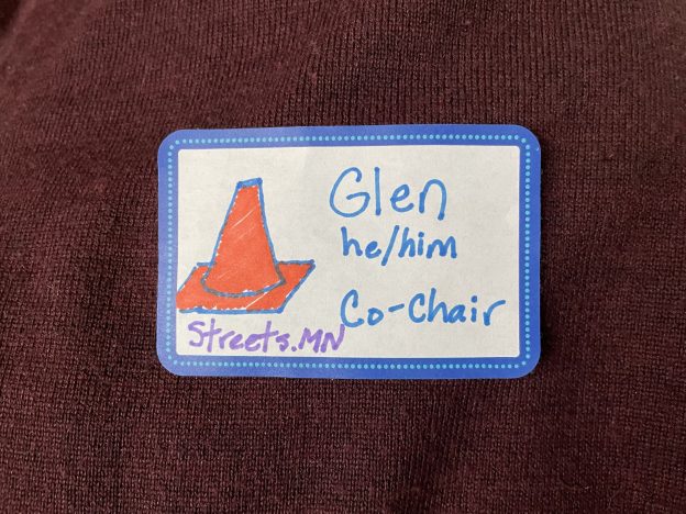 Nametag with a drawn orange traffic cone and words Glen, he/him, Co-Chair, and Streets.mn