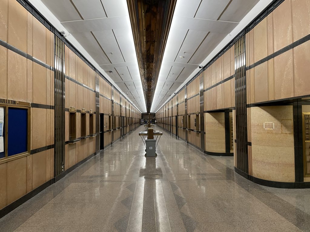 Long hallway with wood paneled walls, shiny gray floor, and alcoves on the right side