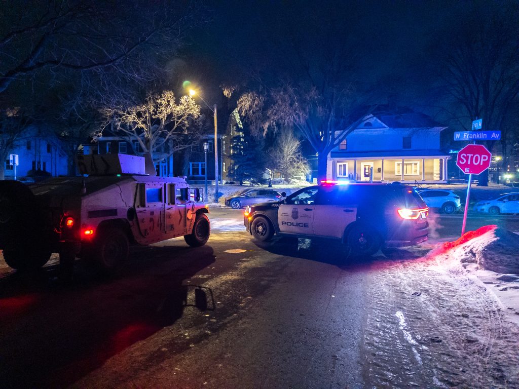 Night time with emergency lights. Minnesota National Guard M1151 vehicle and Minneapolis Police Department Ford Edge SUV at West Franklin Avenue and Pillsbury Avenue on January 24, 2026.