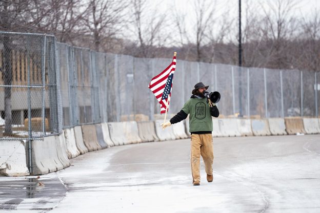 Protester William Kelly Dawokefarmer holding an upside down American flag and a megaphone while protesting at the Bishop Whipple Federal Building.