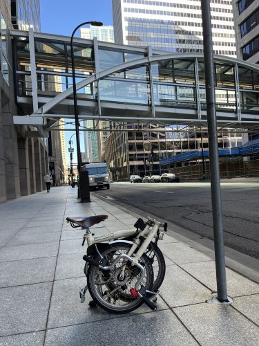 A foldable Brompton bike rests on a sidewalk in downtown St. Paul.
