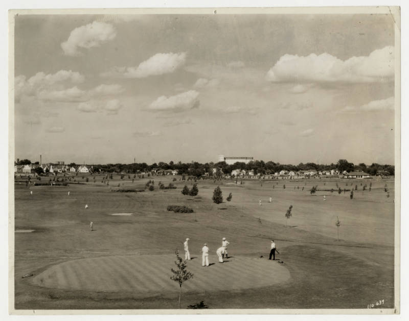 A wide expanse of golf course, with several golfers in the foreground.