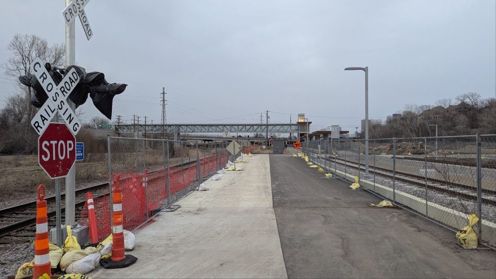 A concrete platform separated from railroad tracks on each side by a chain-link fence.