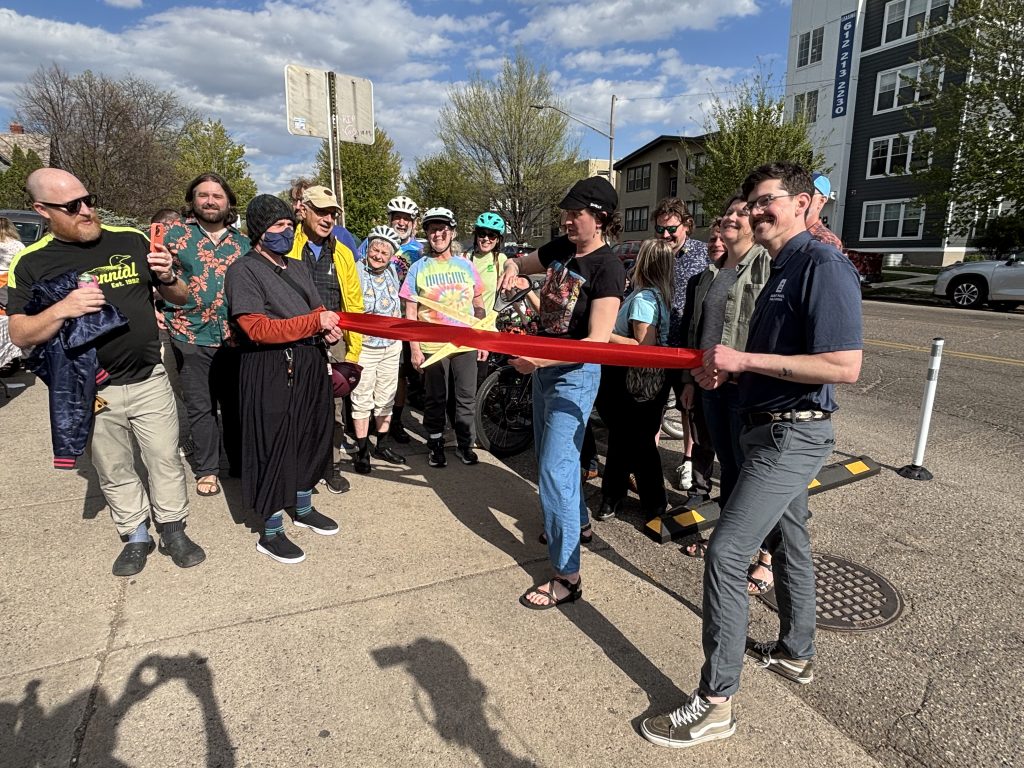 Sarah Johnson cuts a red ceremonial  ribbon in front of a crowd along Grand Avenue. 