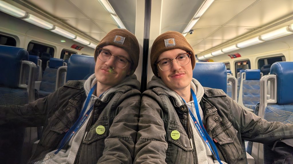 NJ Hanson leans against a window of a commuter train at night with a mirror image reflecting back on the left