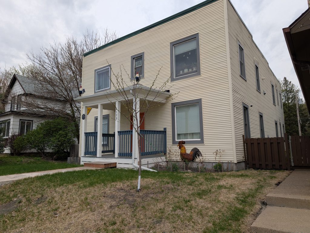 boxy residence with two metal roosters on front porch roof and one in lawn