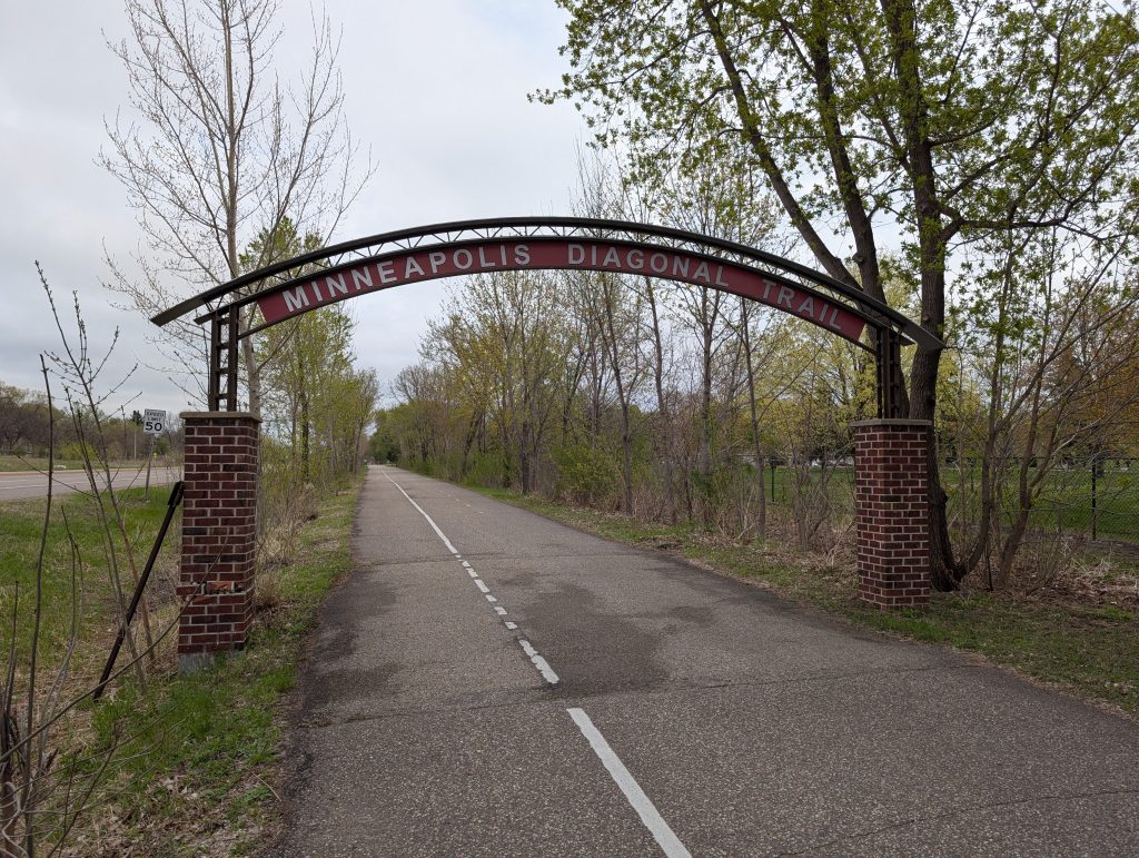 Curved sign saying "Minneapolis Diagonal Trail" over trail