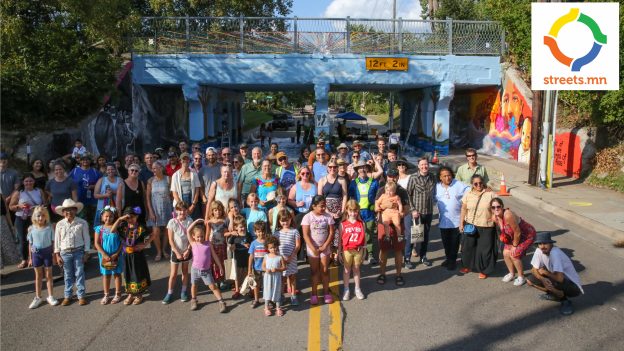 A large crowd standing in front of a bridge with a mural painted on it.