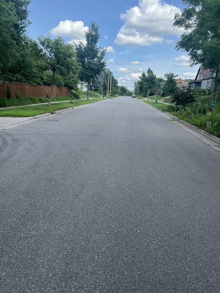 A wide stretch of asphalt on 34th Street, with a single car parked along the curb in the distance.