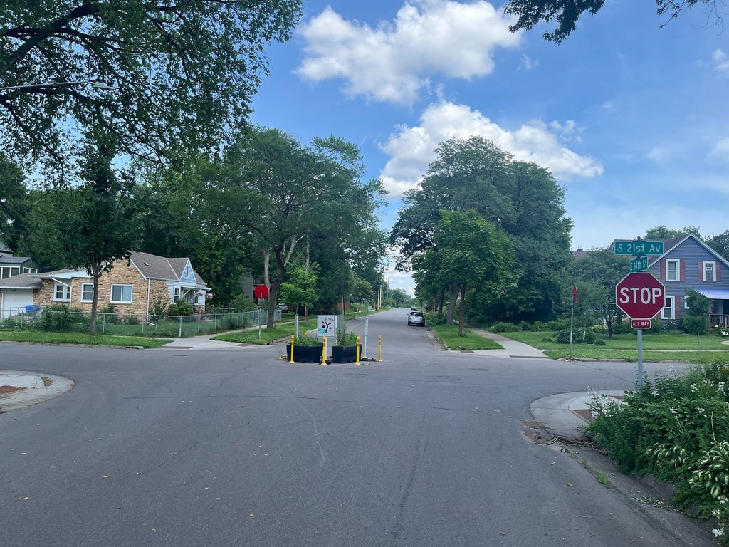 A view of a quick-build traffic circle, consisting of planter boxes and flexposts, at a residential intersection.