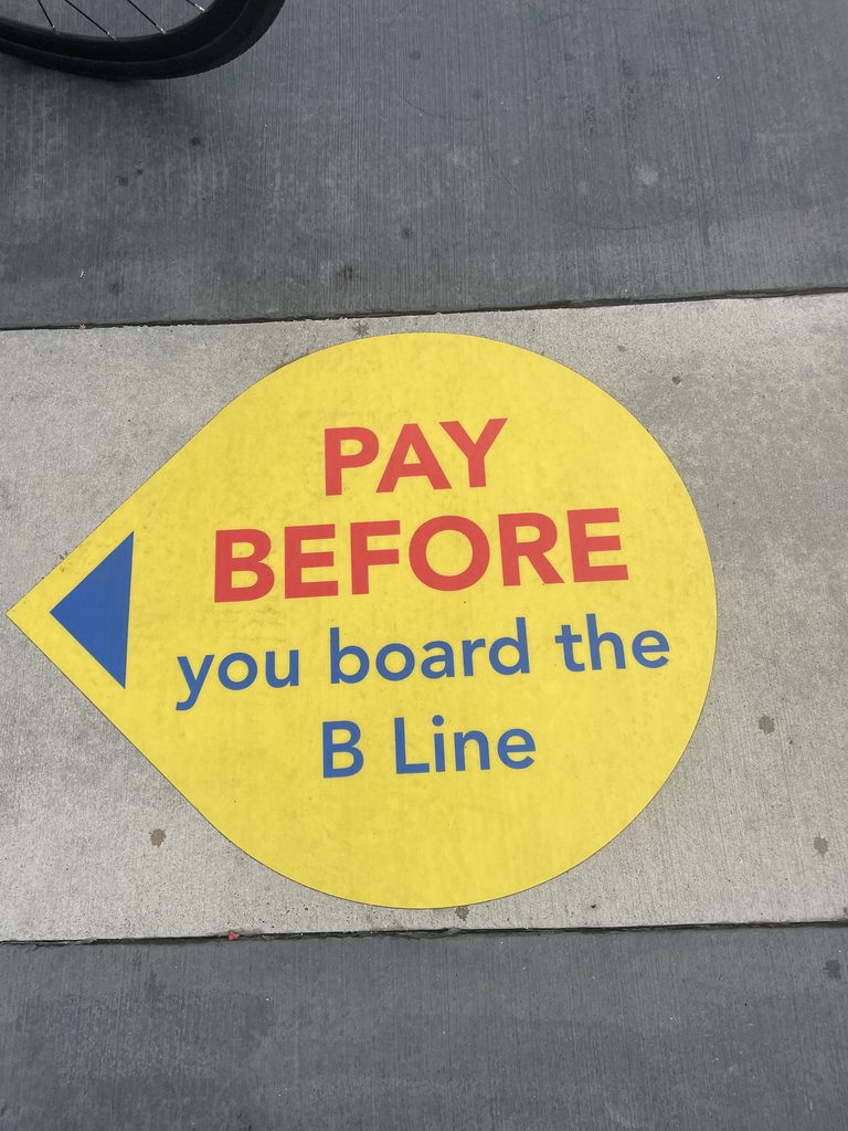 Painted sidewalk sign: Pay before you board the B Line.