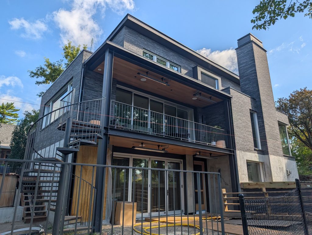 boxy house faced in dark grey brick with spiral staircase and two-level patio