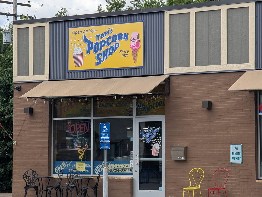 storefront signed "open all year Tom's Popcorn Shop since 1971" with illustrations of popcorn and an ice cream cone