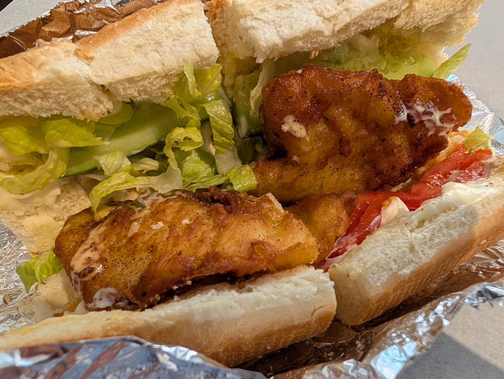 sandwich cut in half with fried fish and shredded lettuce as the most prominent ingredients