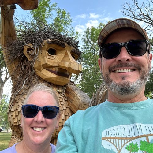 Jan and her husband pose in front of a larger-than-life wooden sculpture of a troll.
