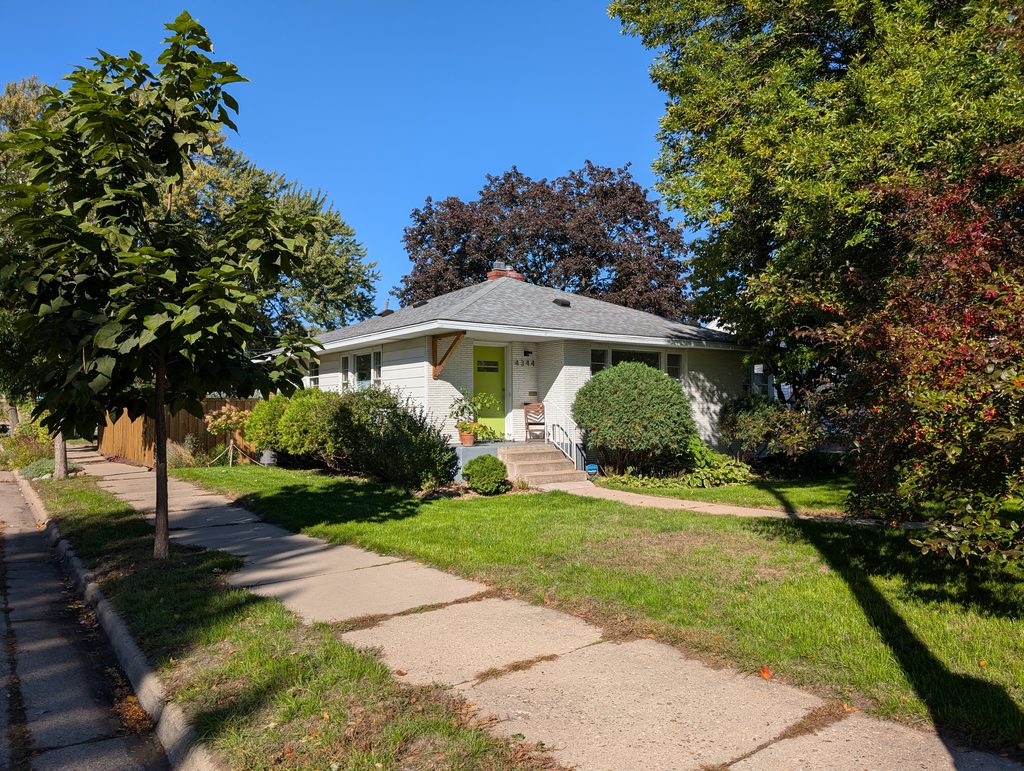 light colored one-story house with green door surrounded by trees and bushes