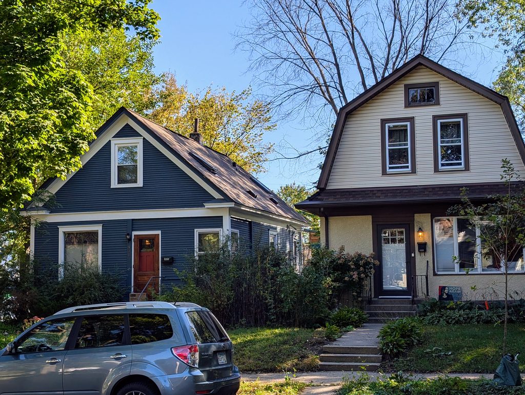 blue sided house with triangular upper level framed in cream-colored trim next to cream-sided house with brown trim and a barn-like upper level formed by steeper roof at the sides than on top