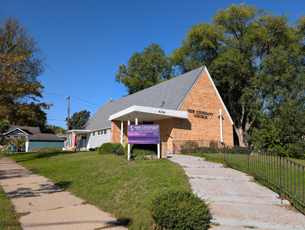 sunlit church with brick face between steep roof sides; a purple sign is in front